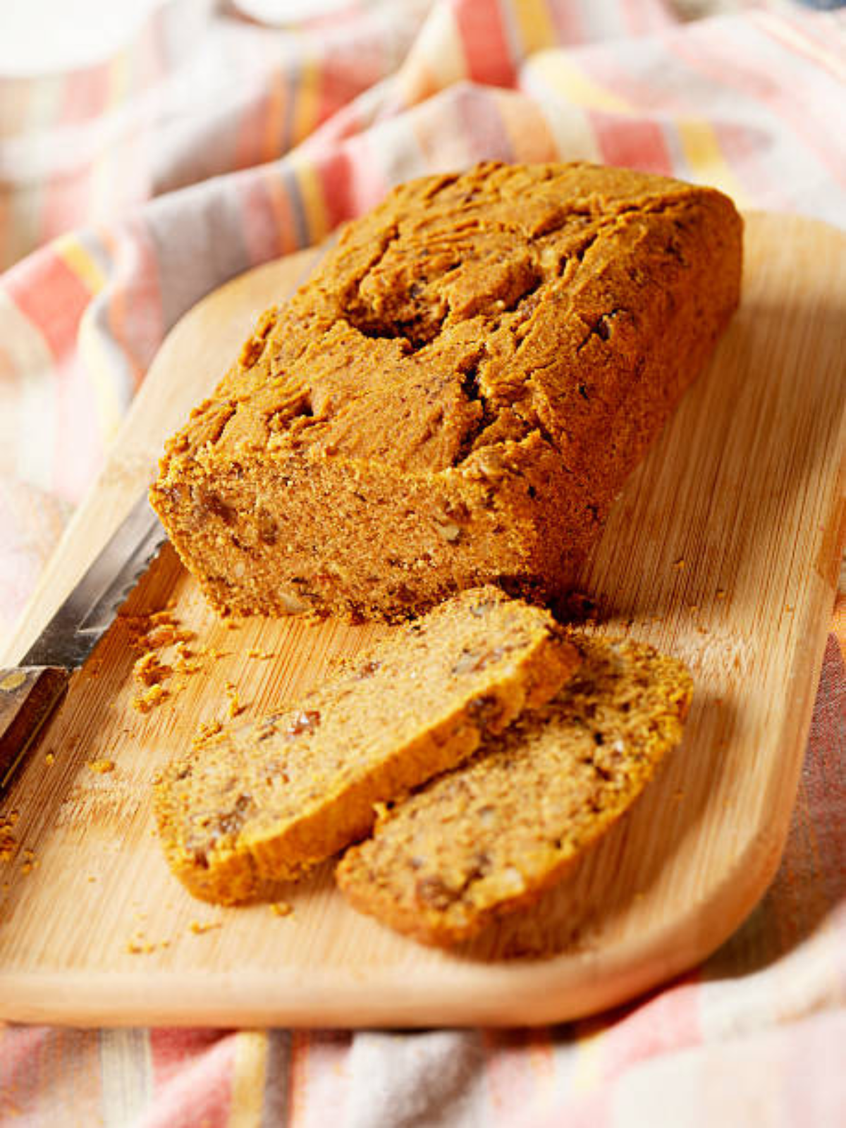 A whole baked sugar-free pumpkin spice bread loaf placed on a wooden board next to a bread knife.
