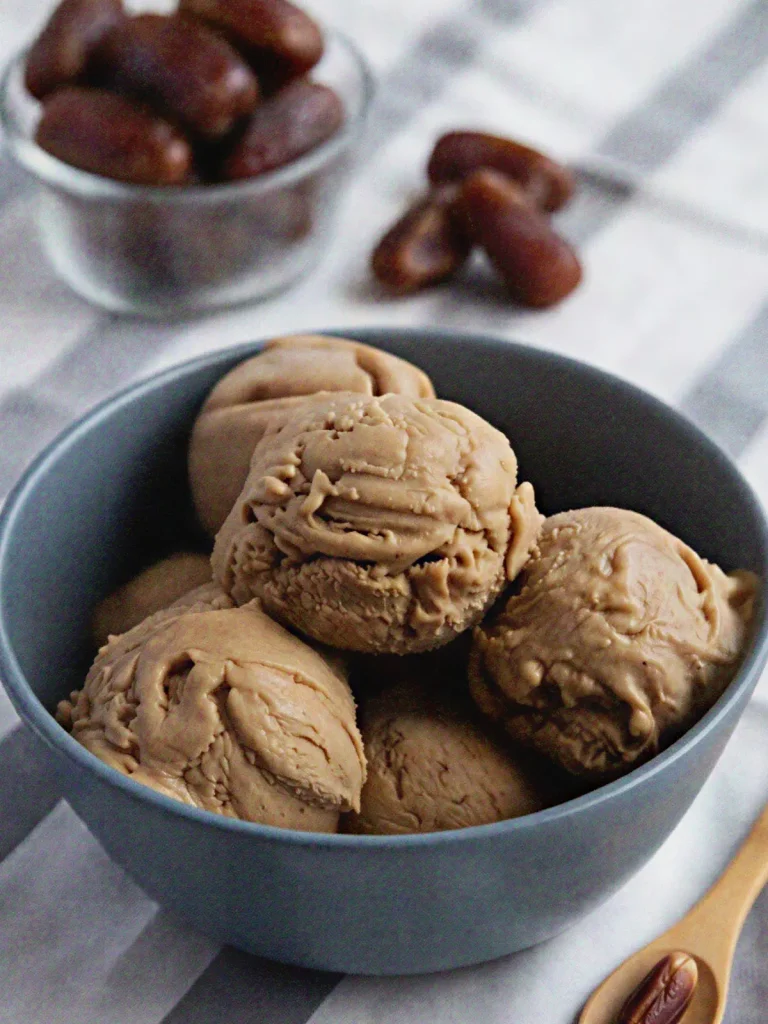 A gray bowl filled with scoops of creamy date sweetened ice cream served with whole Medjool dates on the side.